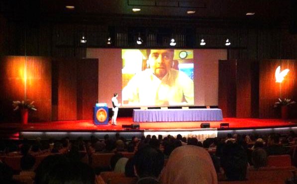 Konferans salonu; sahnedeki büyük ekranda Abdullah Özel konuşuyor